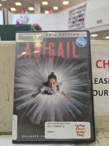 Dvd copy of 2024 film abigail showing the titular character in ballet outfit with blood stains sitting on checkout cart at cabell county library